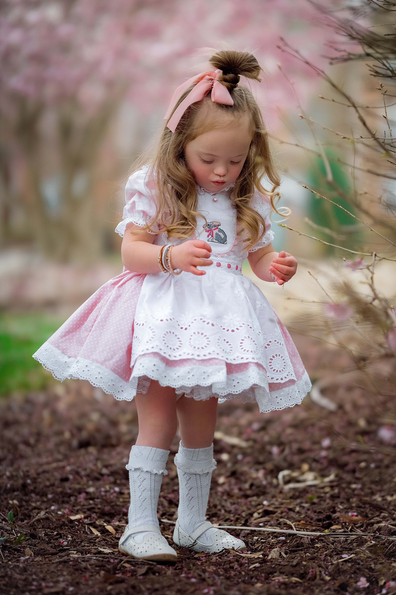 A young girl in a pink and white dress plays in a park with pink tree blossoms Children’s Boutique Raleigh NC