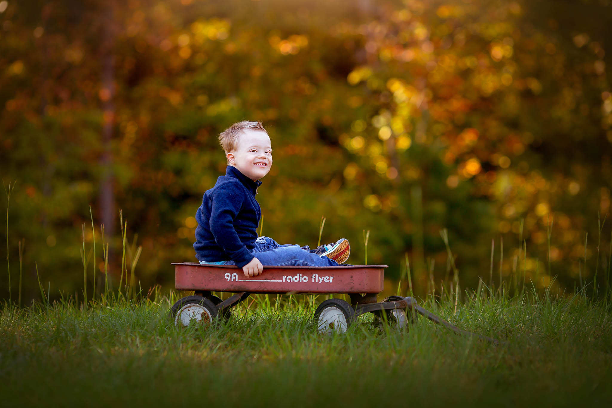 a little boy with down syndrome plays in a red wagon