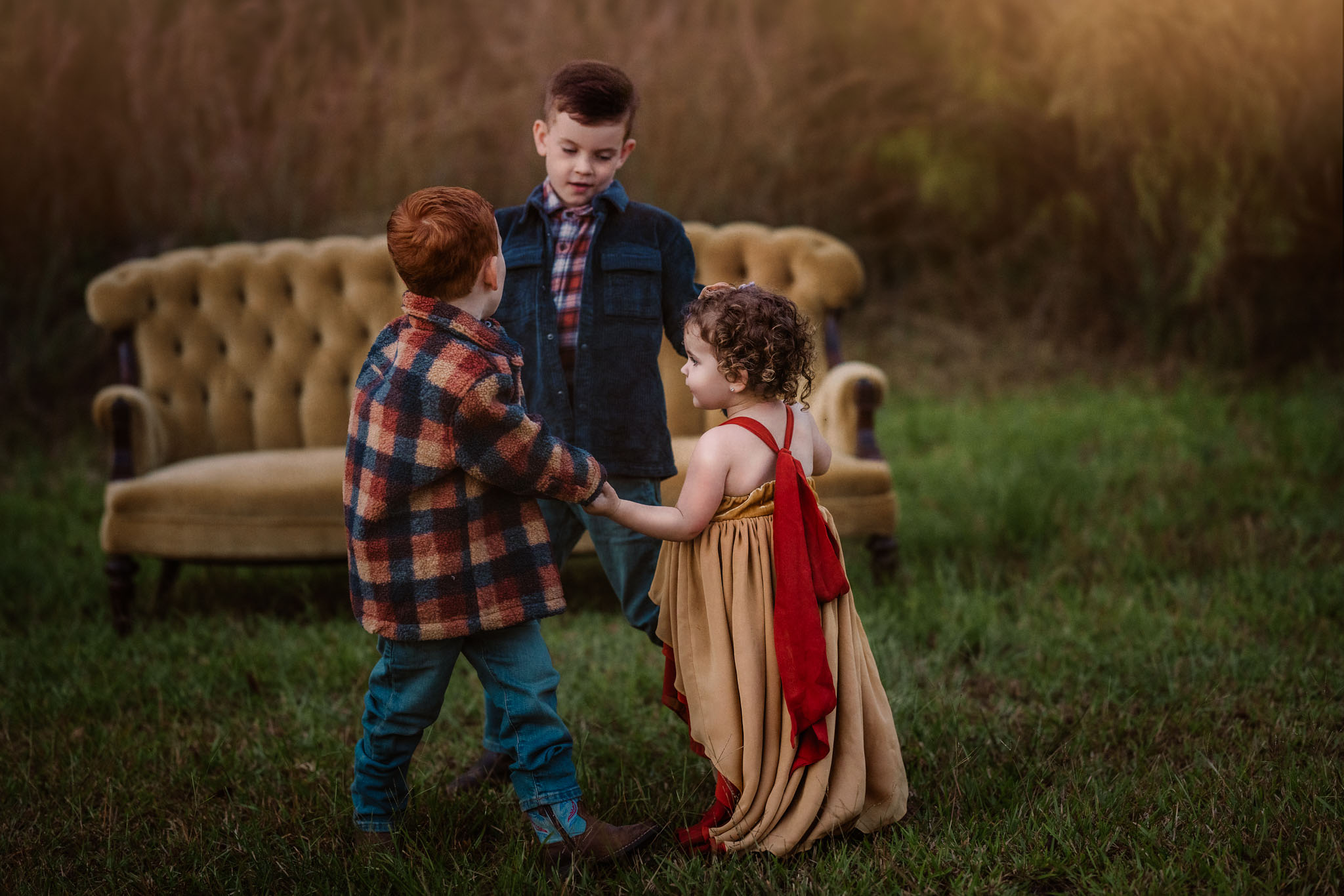 Three siblings hold hands and play together in a grassy field in front of a couch raleigh toy stores