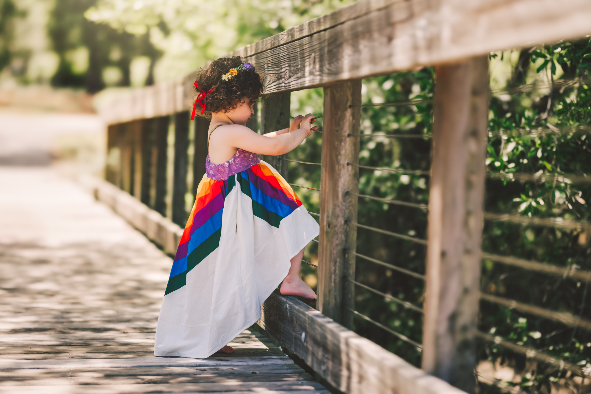 little girl in a rainbow dress playing on a bridge