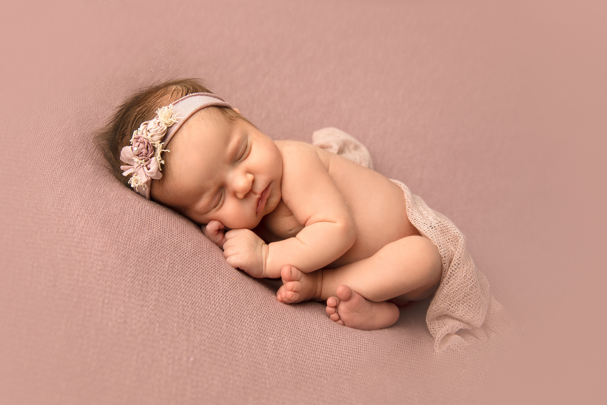 A newborn baby sleeps on a pink pad in a fabric headband raleigh nannies