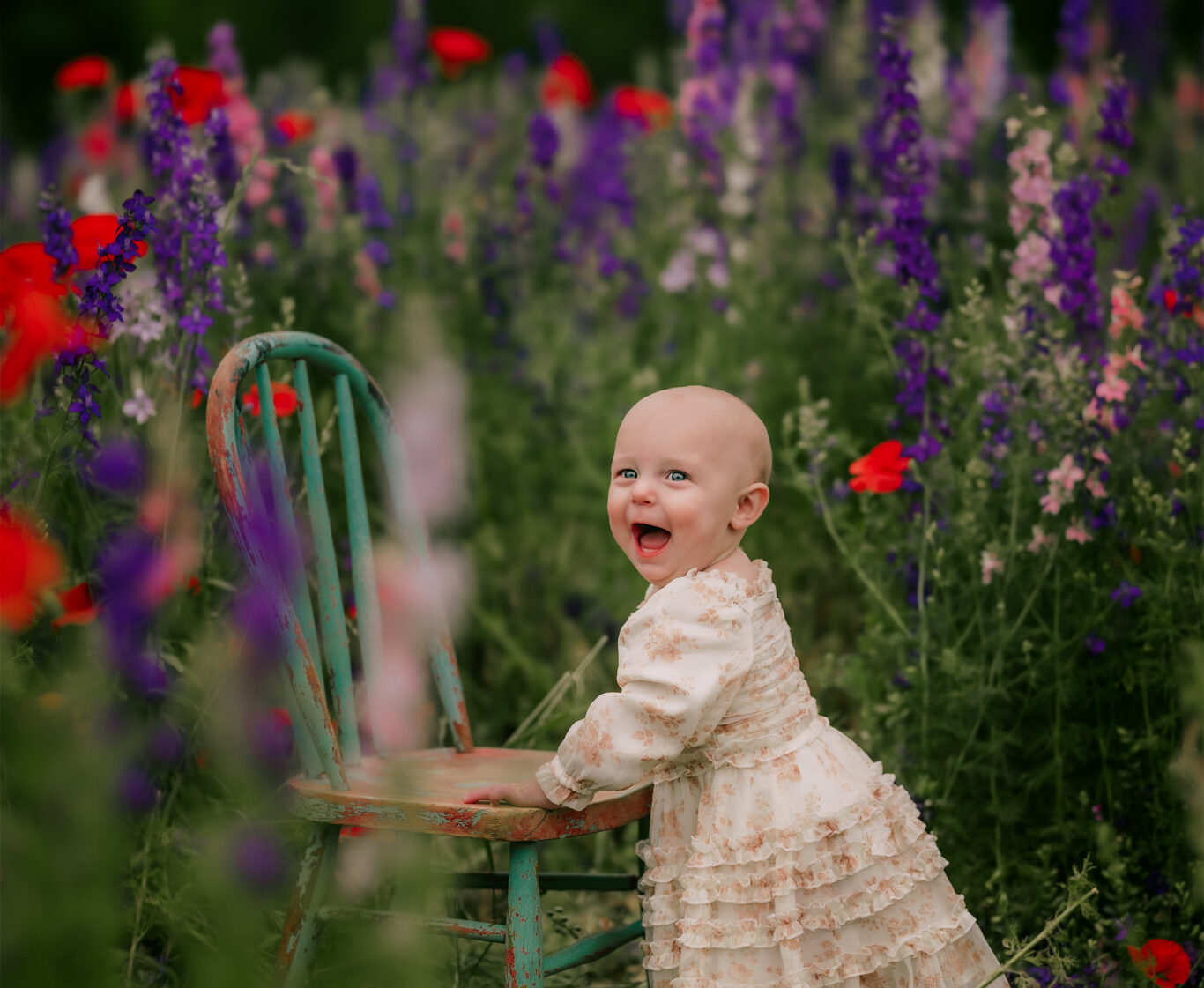 baby girl standing next to a small chair in the flowers