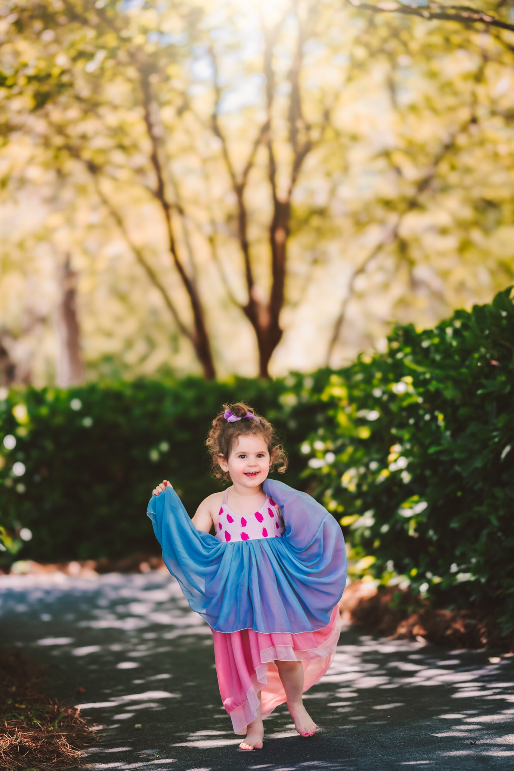 A toddler girl dances in a pink and blue dress in a park path raleigh dance classes