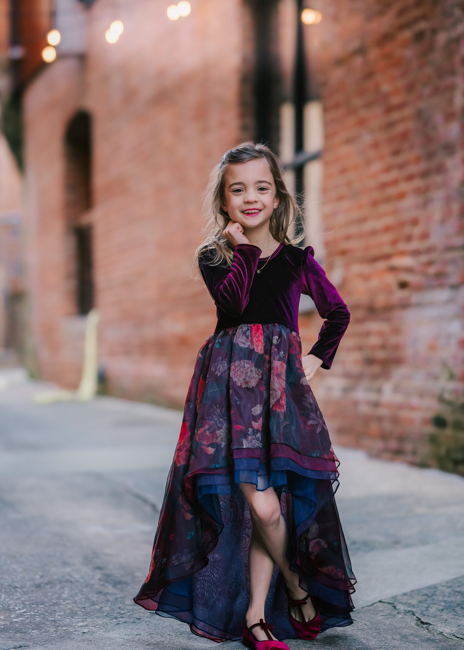 A young girl in a purple dance dress stands in a alley with a brick building raleigh youth sports