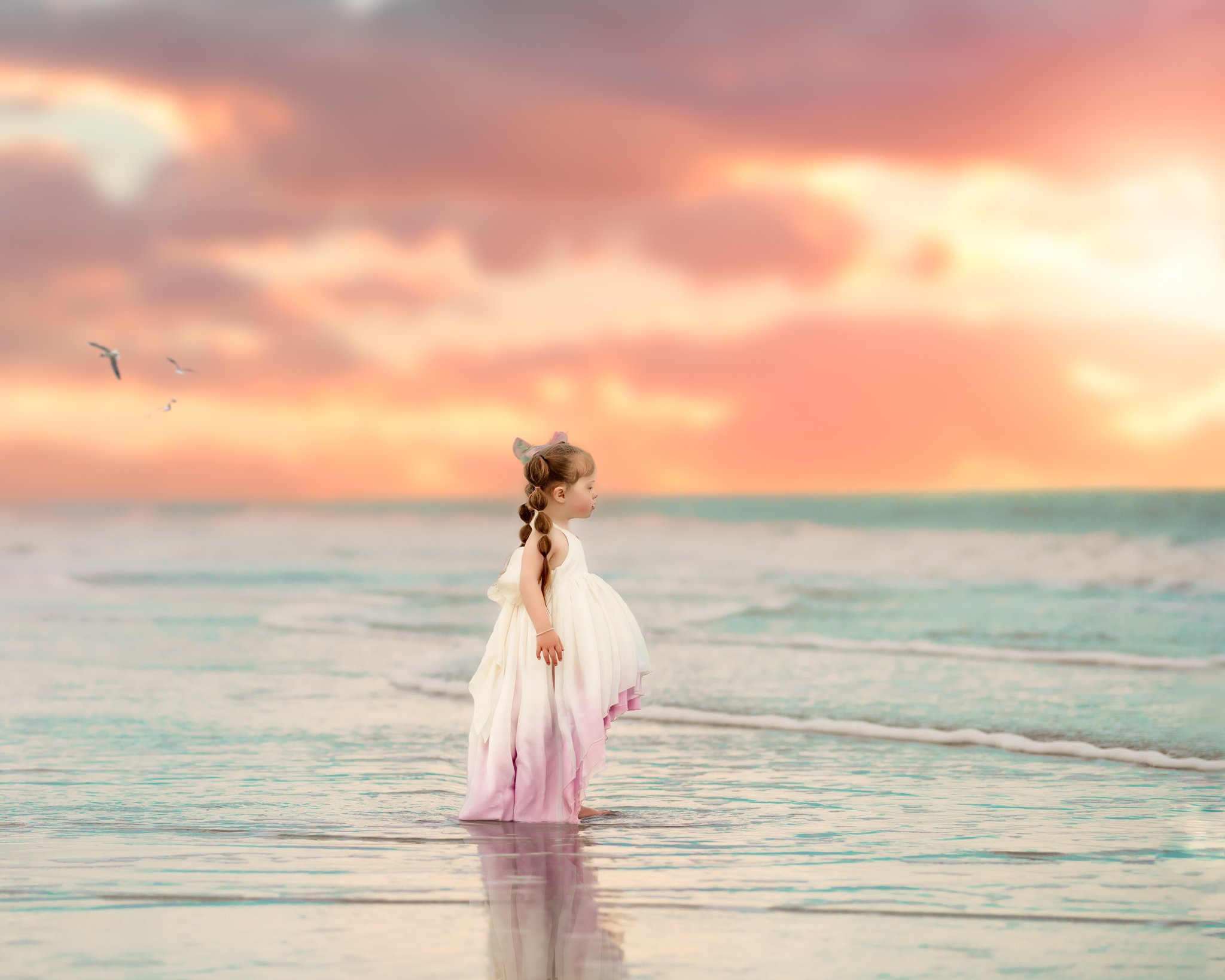 Little girl in a pretty dress standing in the ocean at sunset