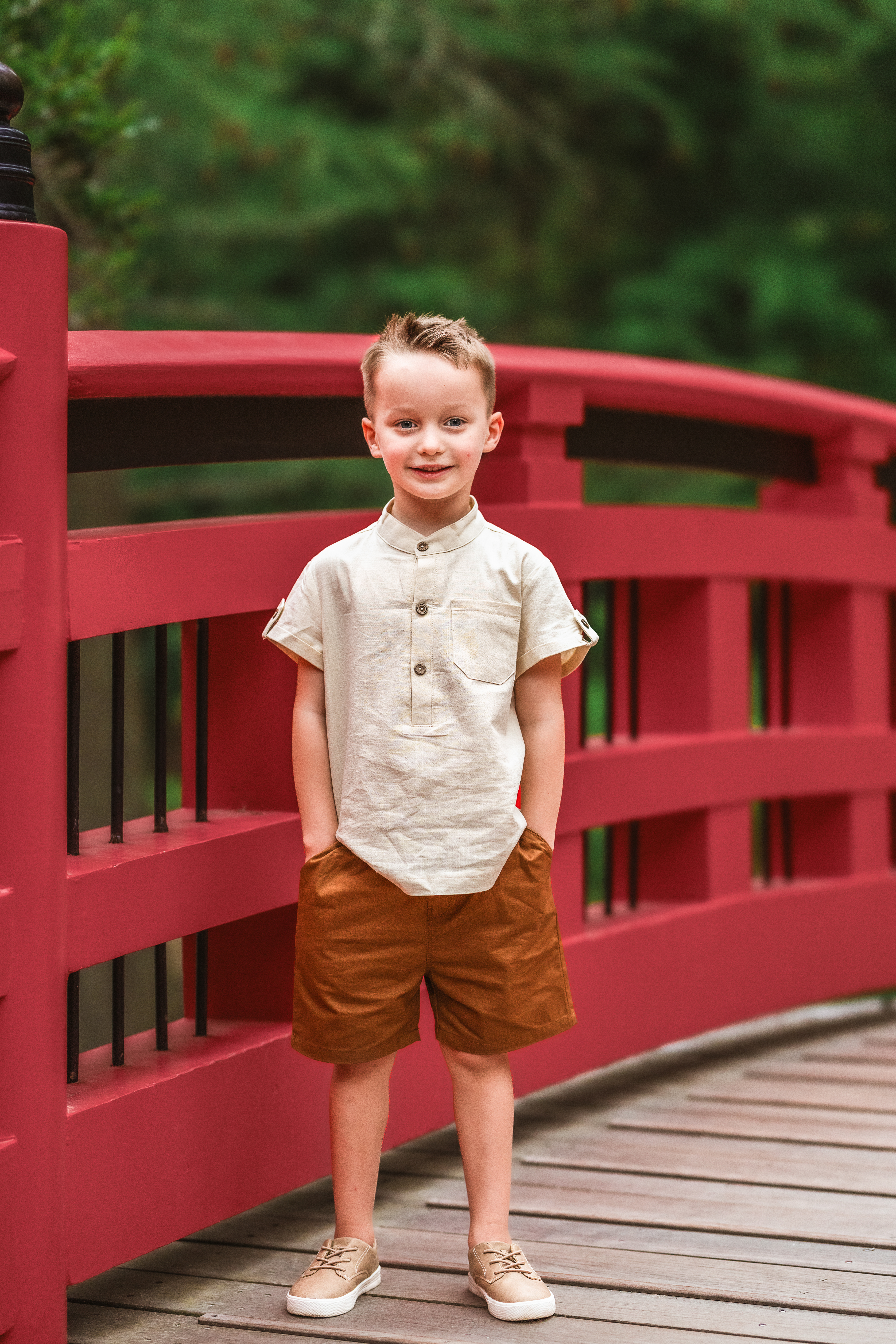 little boy standing on red bridge hands in his pockets