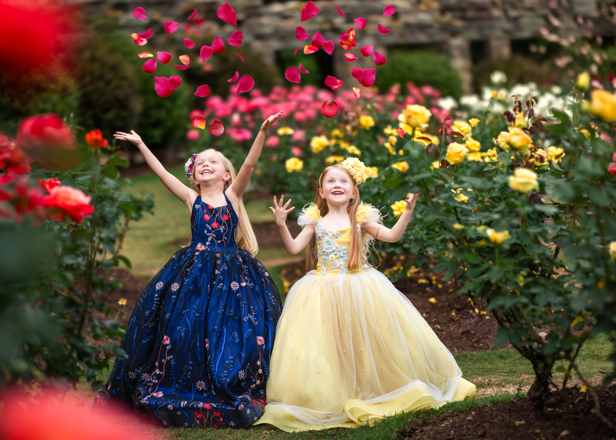 Two little girls in fancy gowns tossing flower petals at the Raleigh Rose Gardens